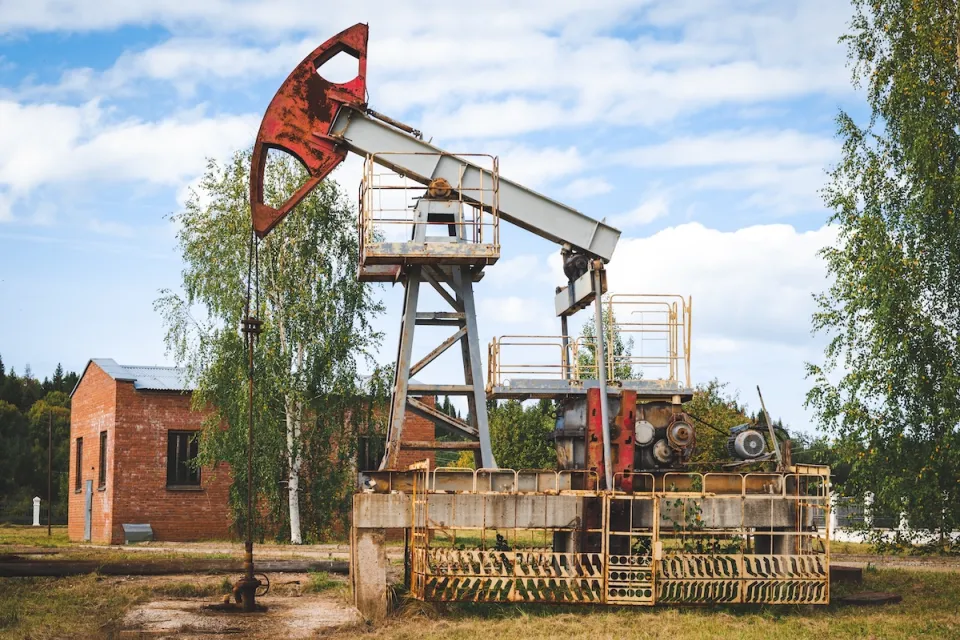 Old oil well with red brick building in the background.